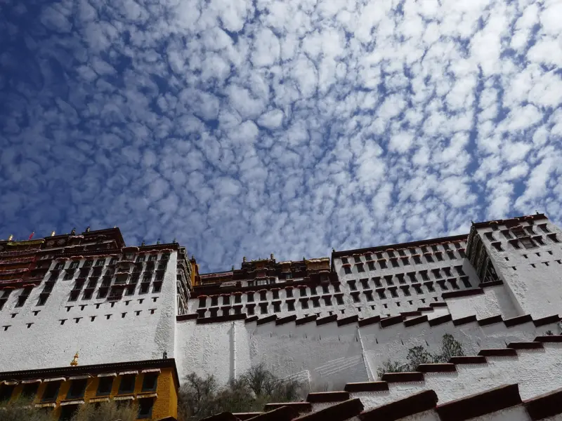 Imposante, weiße Fassade des Potala-Palastes in Lhasa, Tibet, fotografiert von unten gegen den dramatischen Wolkenhimmel.