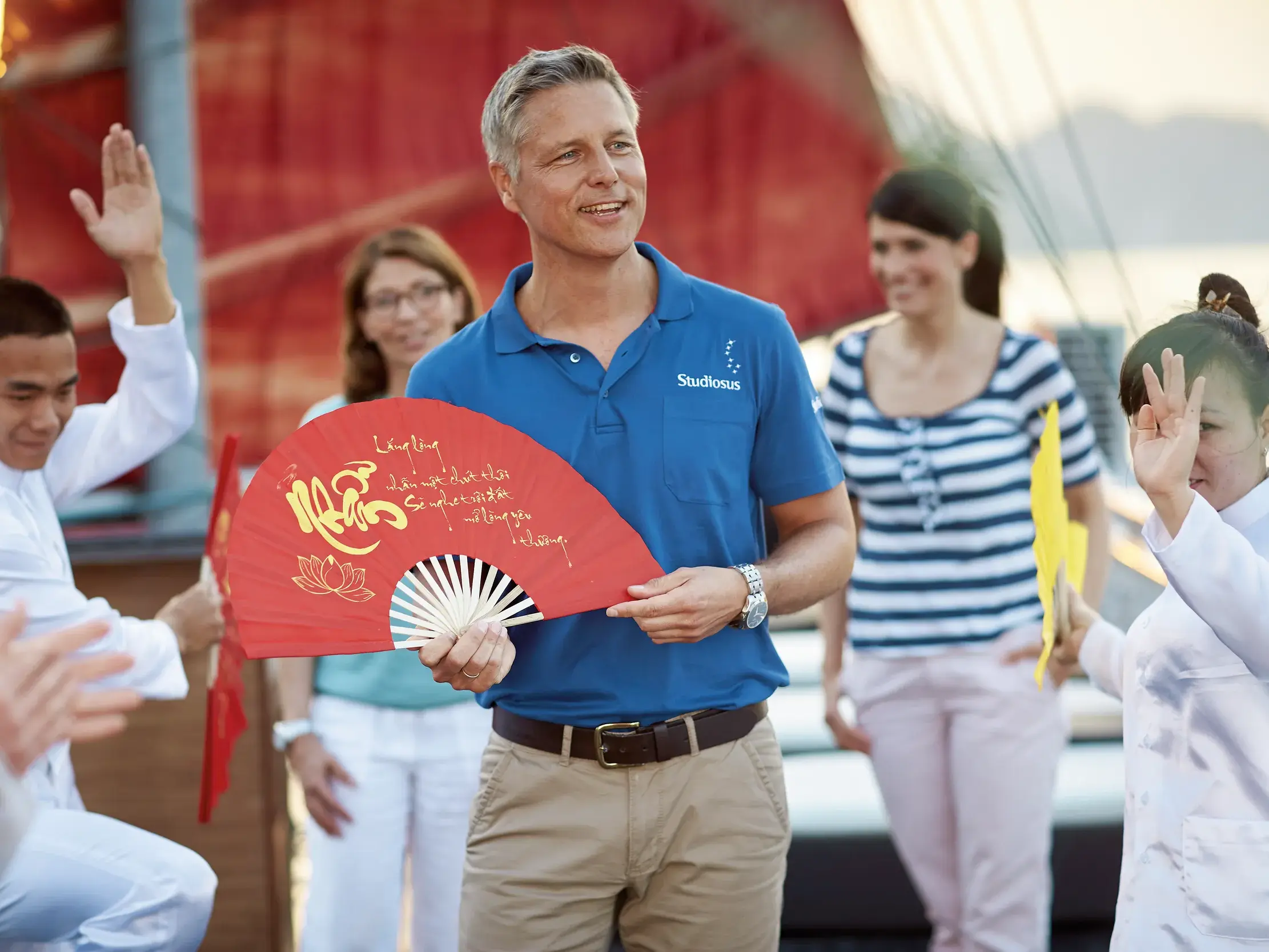 Ein Studiosus-Reiseleiter mit Reisegruppe bei einer kulturellen Vorführung auf dem Deck eines Schiffes in der Halongbucht.