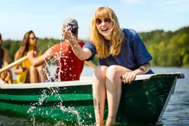 Lachende junge Frau spritzt Wasser vom Bug eines Kanus auf dem Immelnsee während einer Gruppenreise für junge Leute in Südschweden.