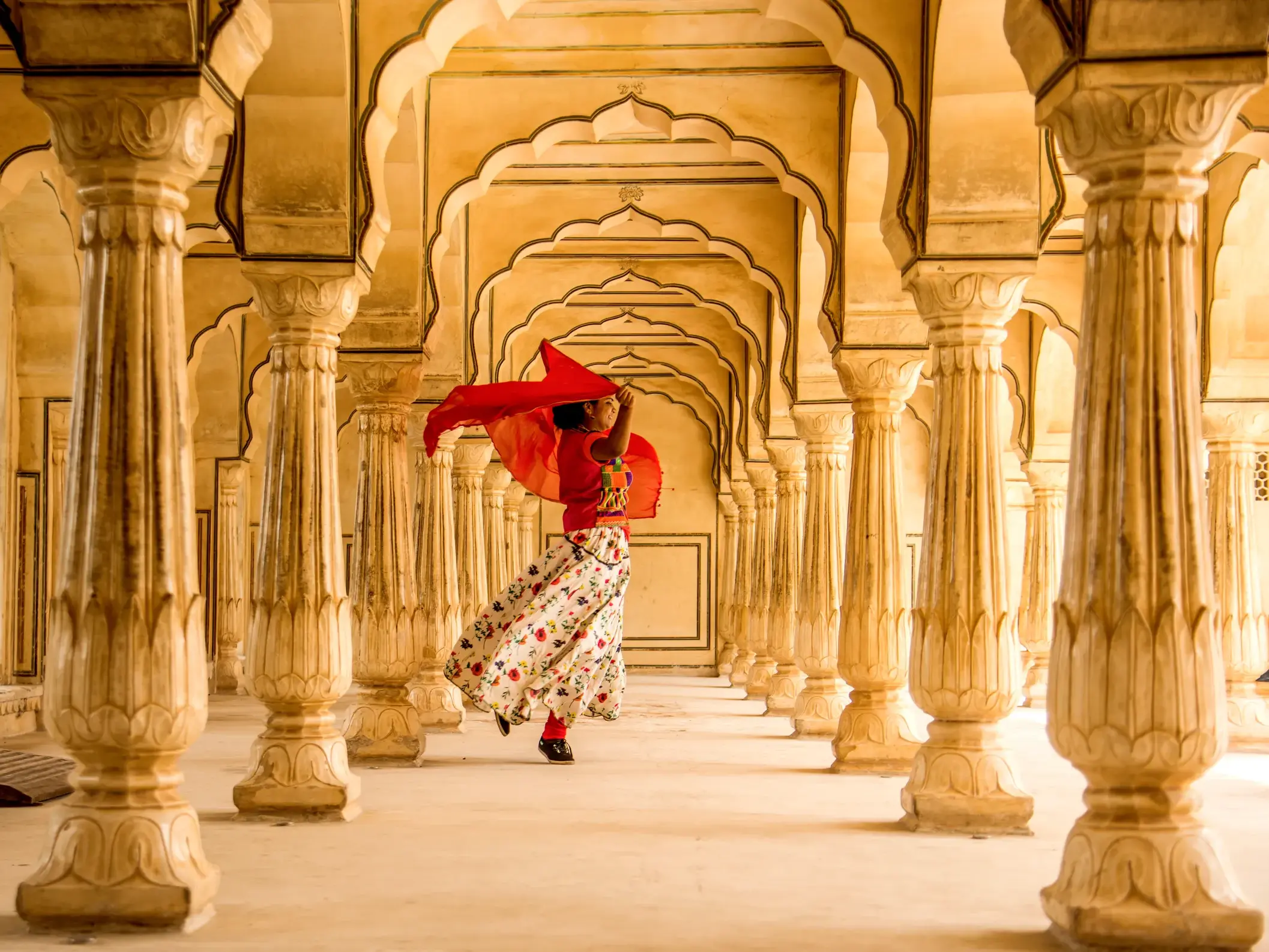 Ein Mädchen tanzt mit einem roten Tuch durch die Säulenhalle im Amber Fort in Jaipur, einem Highlight dieser Indien-Studienreise.