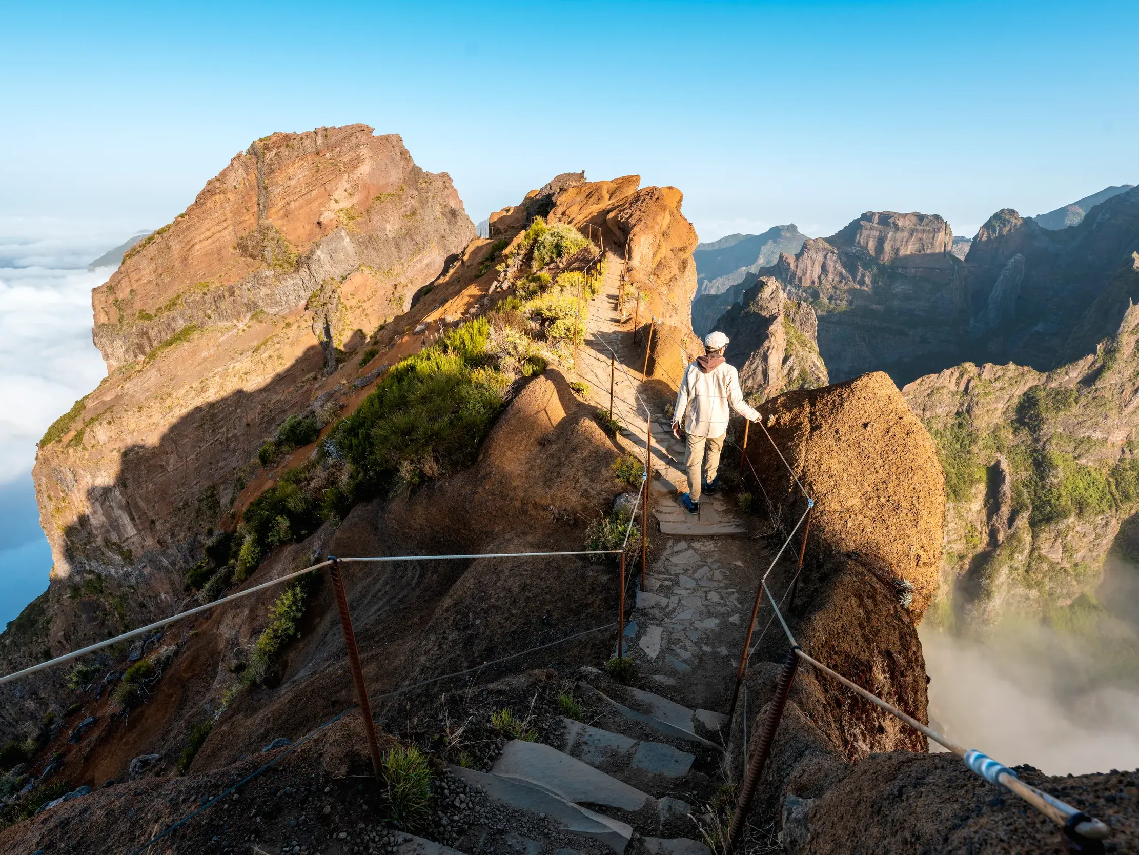Sonnige Gratwanderung auf einem gesicherten Pfad am Pico do Arieiro mit weitem Blick über die schroffe Bergwelt Madeiras.