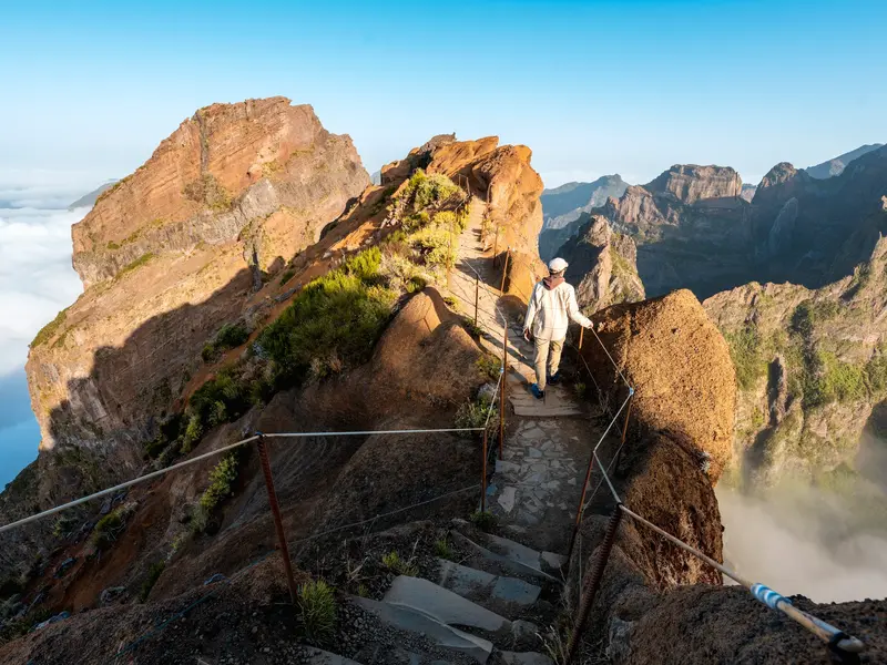 Sonnige Gratwanderung auf einem gesicherten Pfad am Pico do Arieiro mit weitem Blick über die schroffe Bergwelt Madeiras.