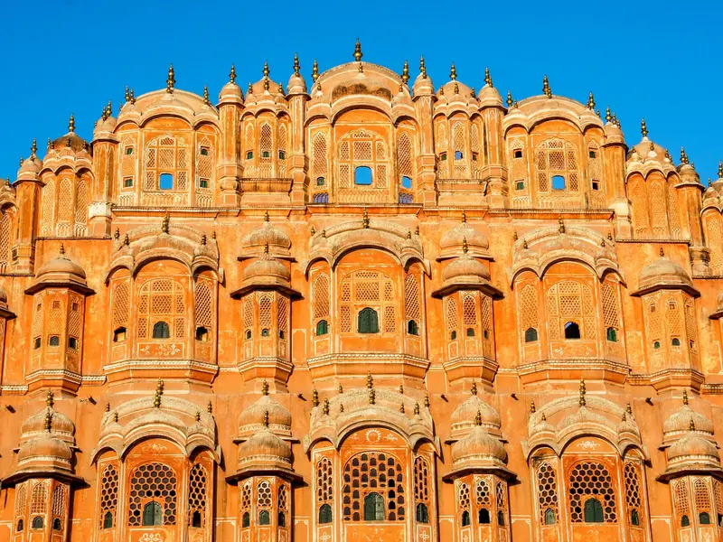 Die beeindruckende, rosafarbene Fassade des Hawa Mahal in Jaipur mit ihren 953 kunstvollen Fenstern unter blauem Himmel.