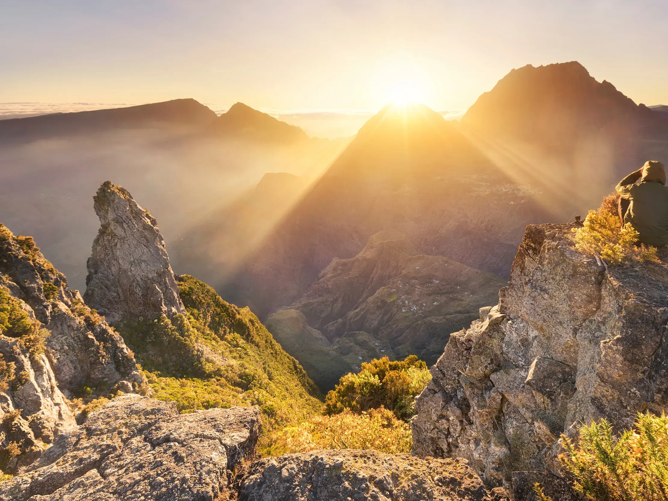 Wanderer genießt den Sonnenaufgang über der nebligen Vulkanlandschaft des Mafate-Talkessels auf La Réunion.