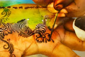 Eine Hand wird kunstvoll mit Zebras und Ornamenten bemalt, eine kreative Darstellung der Safari-Erlebnisse in Tansania.