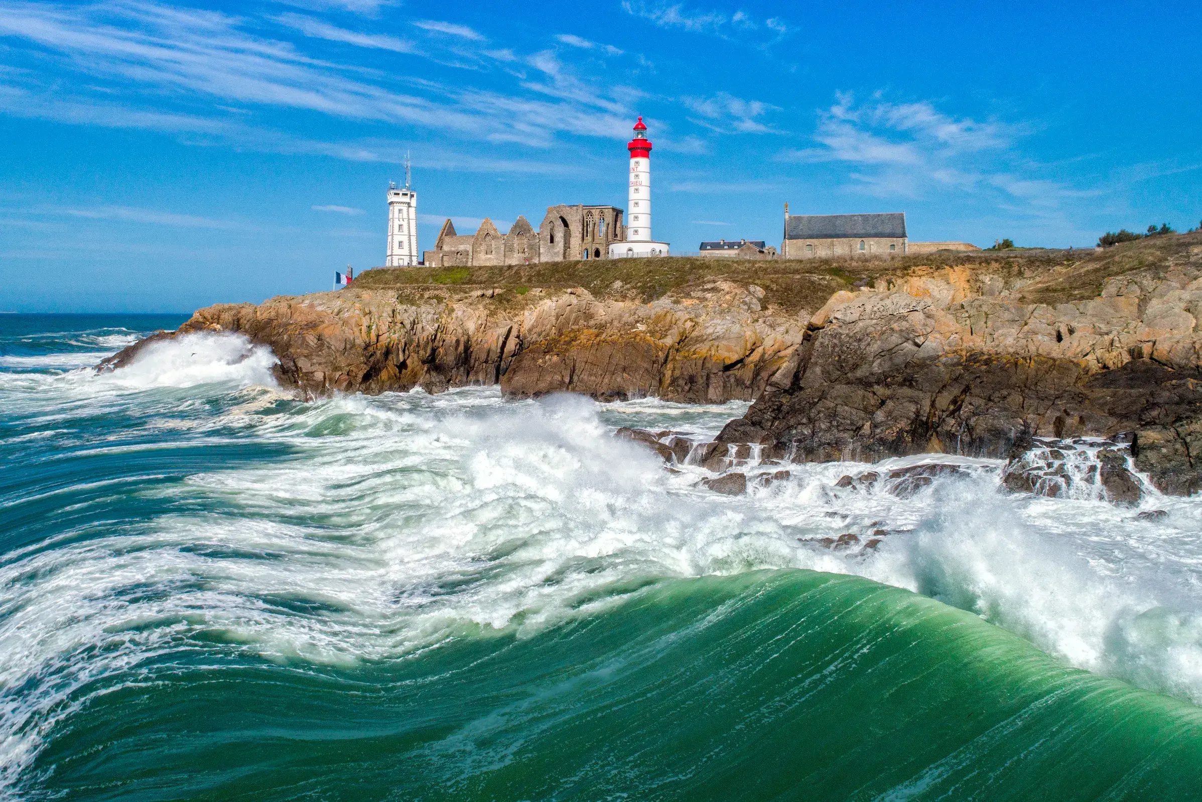 Ein Leuchtturm und eine alte Abtei thronen auf Klippen über den tosenden Wellen der Atlantikküste in der Bretagne.
