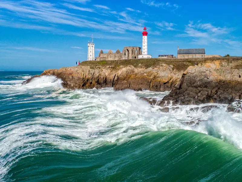 Ein Leuchtturm und eine alte Abtei thronen auf Klippen über den tosenden Wellen der Atlantikküste in der Bretagne.