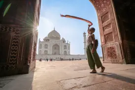 Junge Frau in einem verzierten Torbogen posiert mit einem wehenden Schal vor dem sonnenbeschienenen Taj Mahal in Agra.