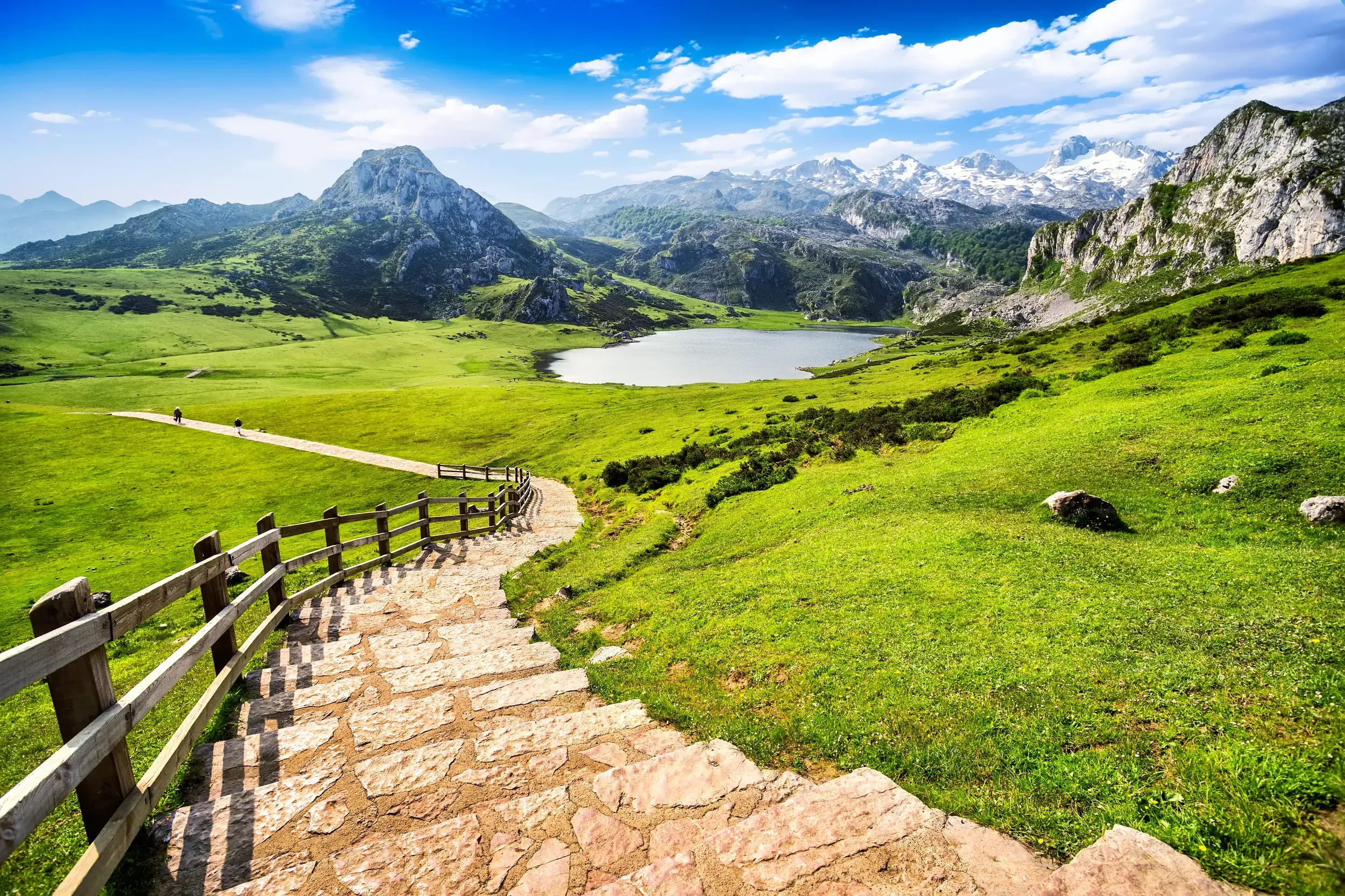 Steinstufen eines Wanderwegs führen hinab in die sattgrüne Landschaft mit Bergseen im Nationalpark Picos de Europa in Nordspanien.