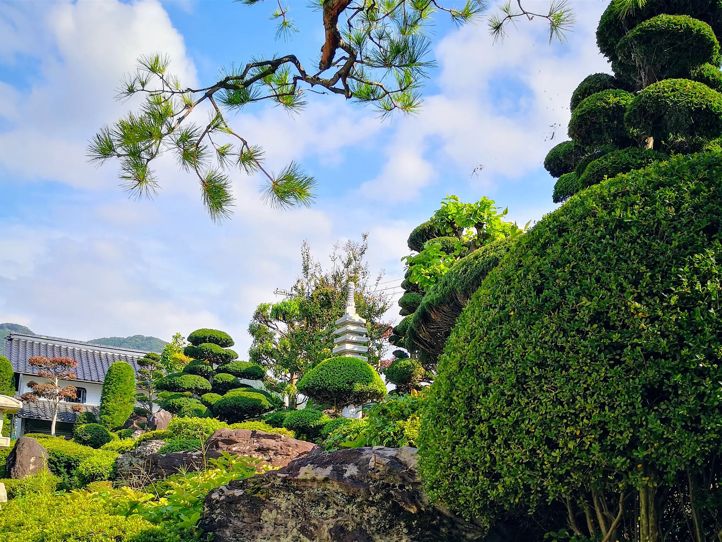 Idyllischer Tempelgarten in Japan mit formgeschnittenen Büschen, Felsen und einer Pagode vor einer Bergkulisse.