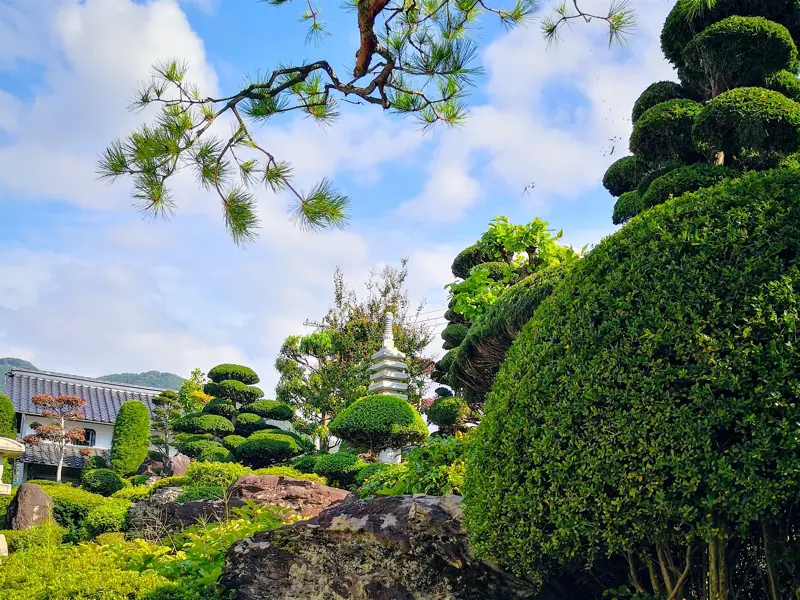 Idyllischer Tempelgarten in Japan mit formgeschnittenen Büschen, Felsen und einer Pagode vor einer Bergkulisse.