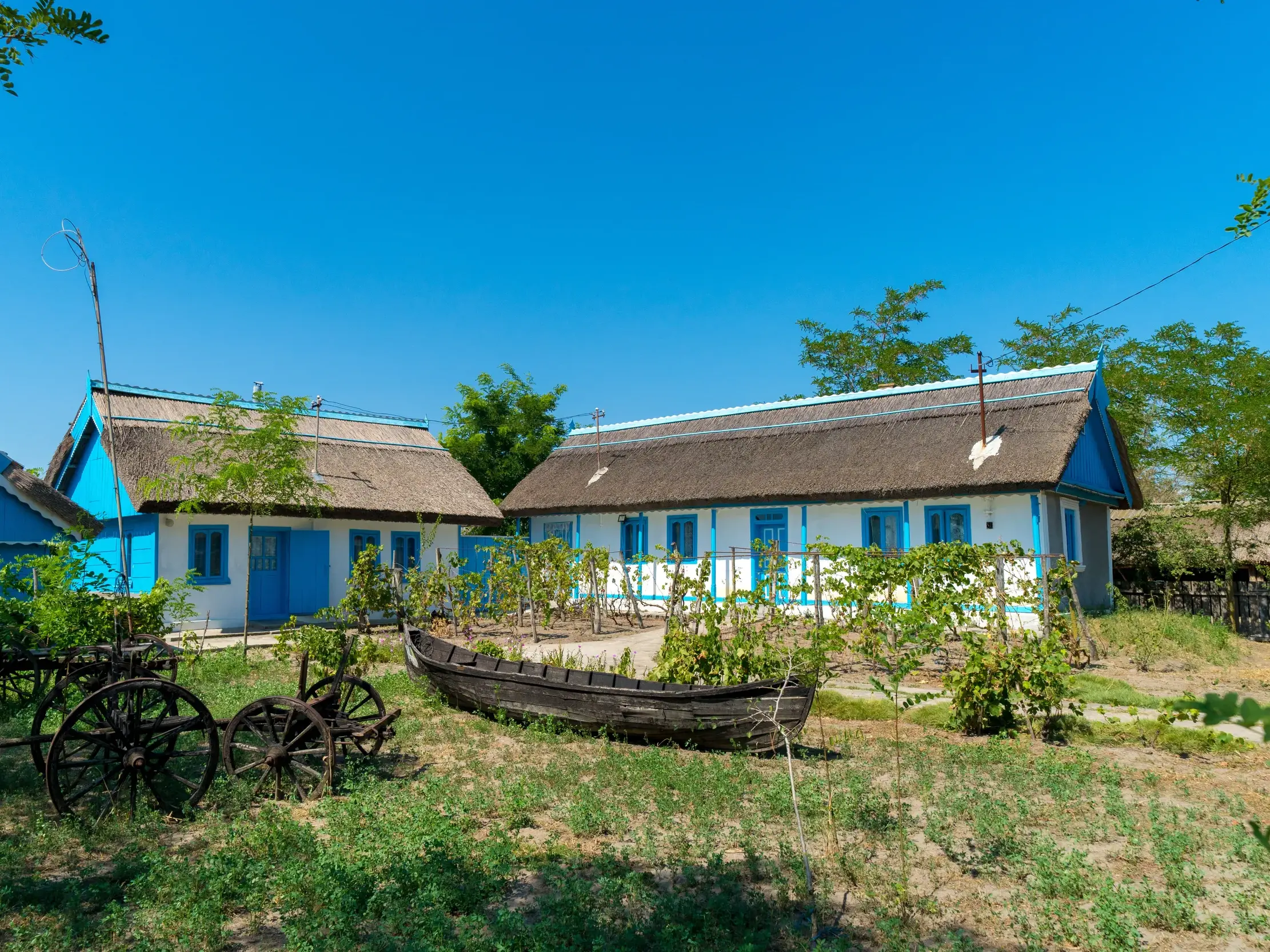Idyllische Pension mit weiß-blauer Fassade und Reetdach im rumänischen Donaudelta, davor ein altes Fischerboot im Gras.