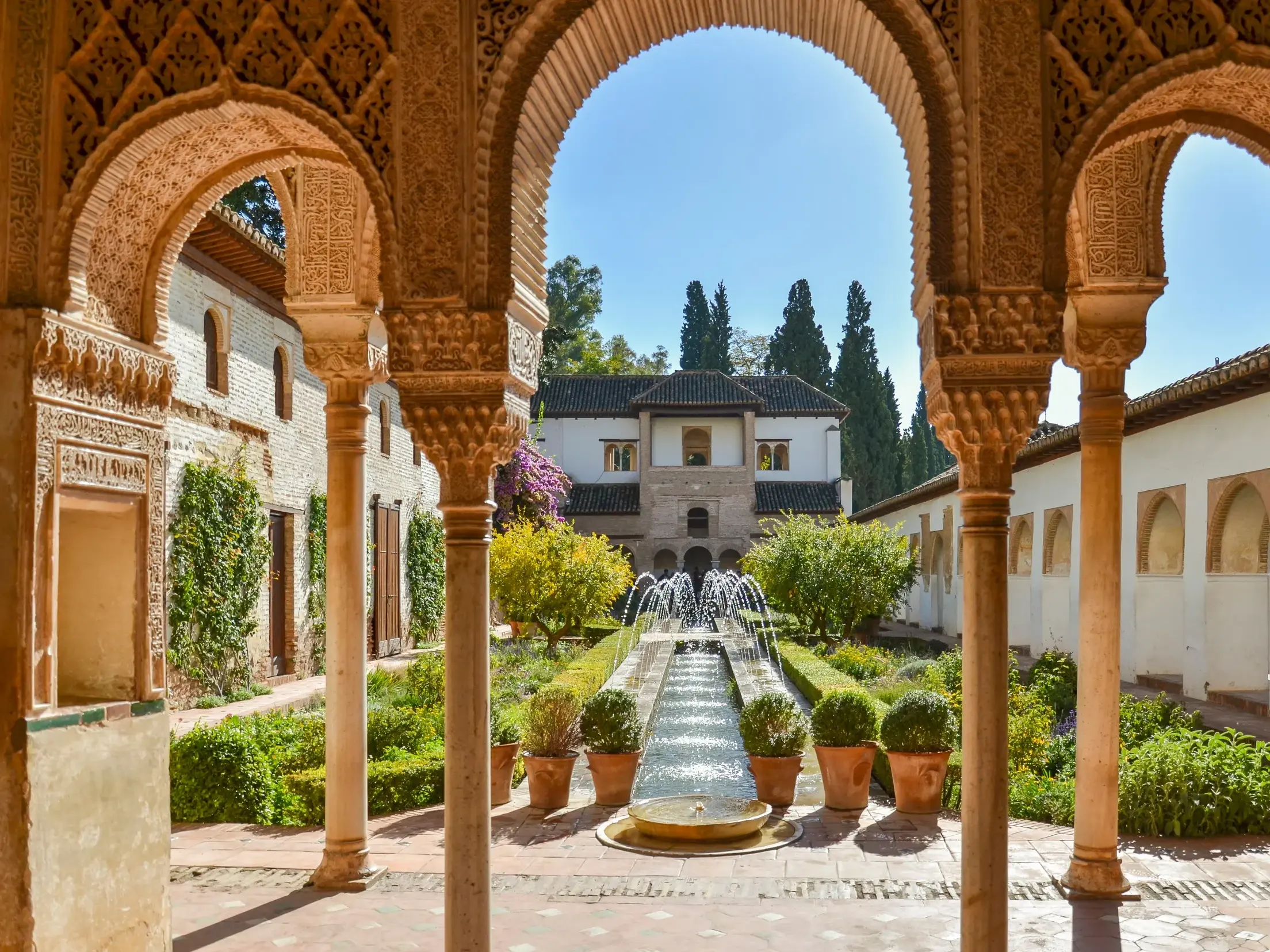 Sonniger Blick durch reich verzierte, maurische Bögen auf den paradiesischen Innenhof der Alhambra in Granada, Andalusien.