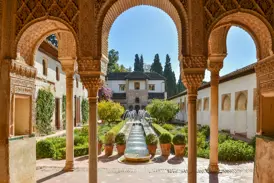 Blick durch die filigranen Bögen der Nasridenpaläste in einen sonnigen Innenhof mit Garten und Wasserspielen in der Alhambra.