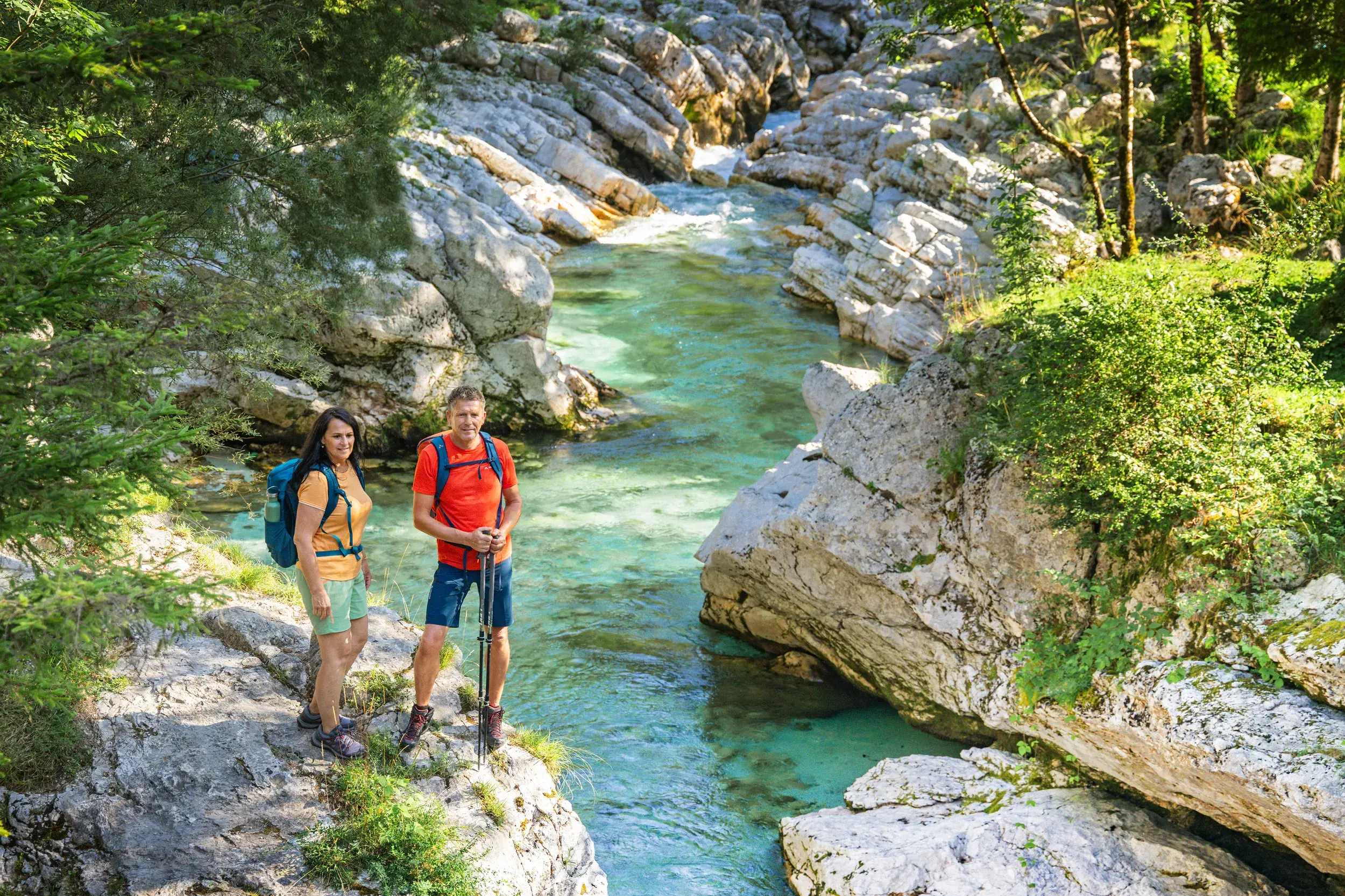 Zwei Wanderer pausieren auf einem Felsen über der smaragdgrünen Soča während einer Wanderreise im Soča-Tal in Slowenien.