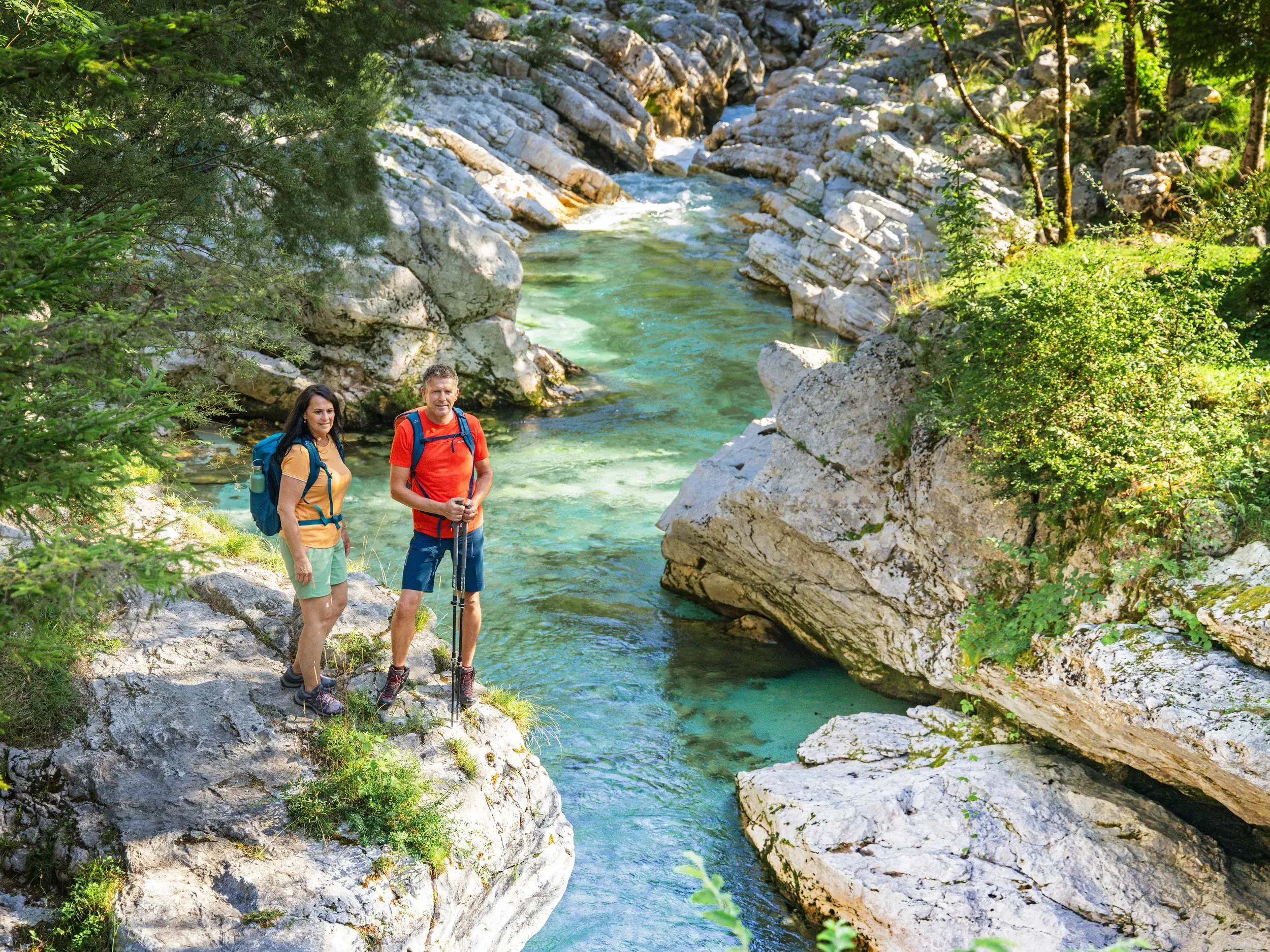 Zwei Wanderer pausieren auf einem Felsen über der smaragdgrünen Soča während einer Wanderreise im Soča-Tal in Slowenien.