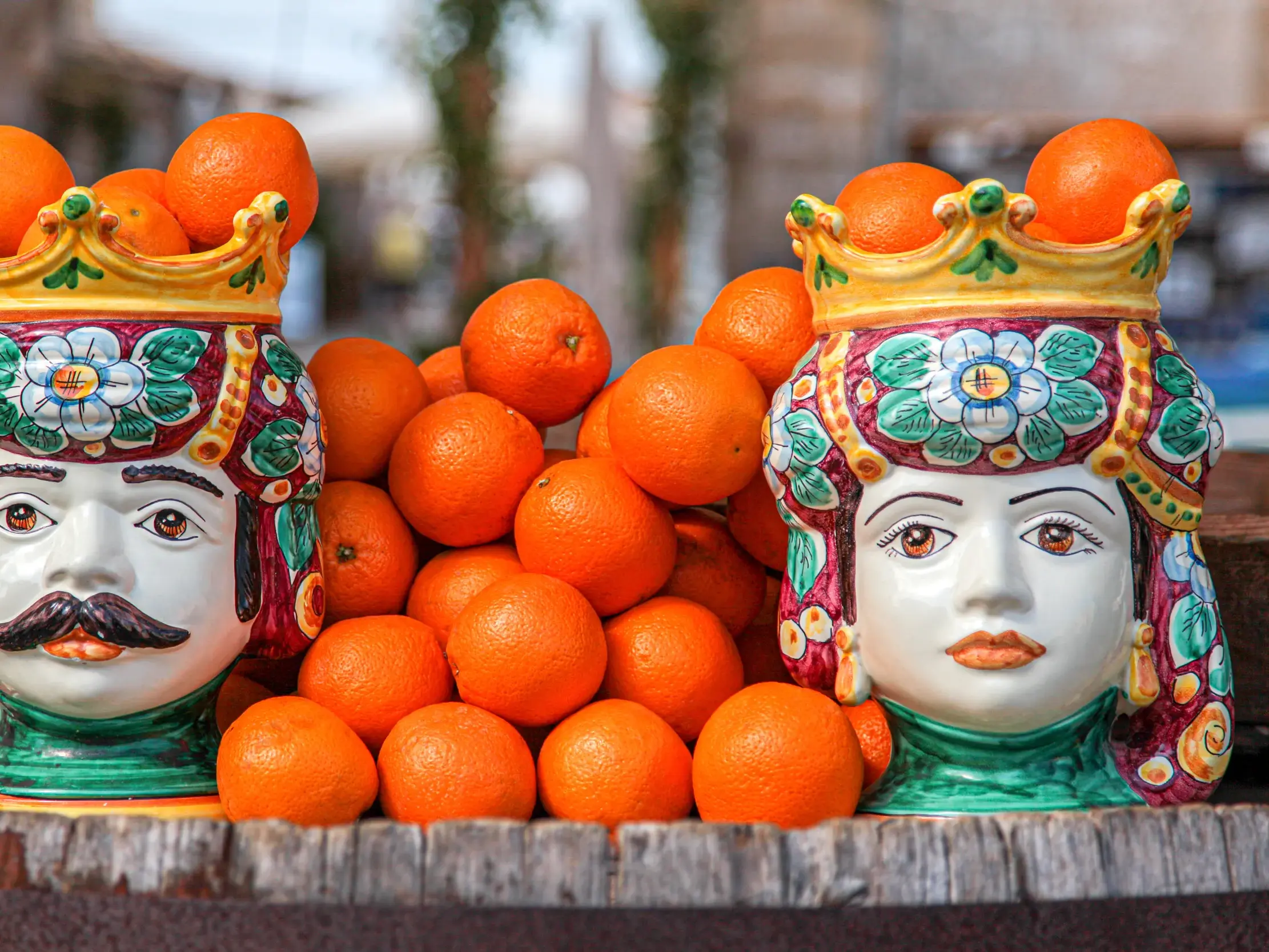 Traditionelle sizilianische Keramikköpfe, „Teste di Moro“, stehen auf einem Holzfass und sind mit frischen Orangen gefüllt.