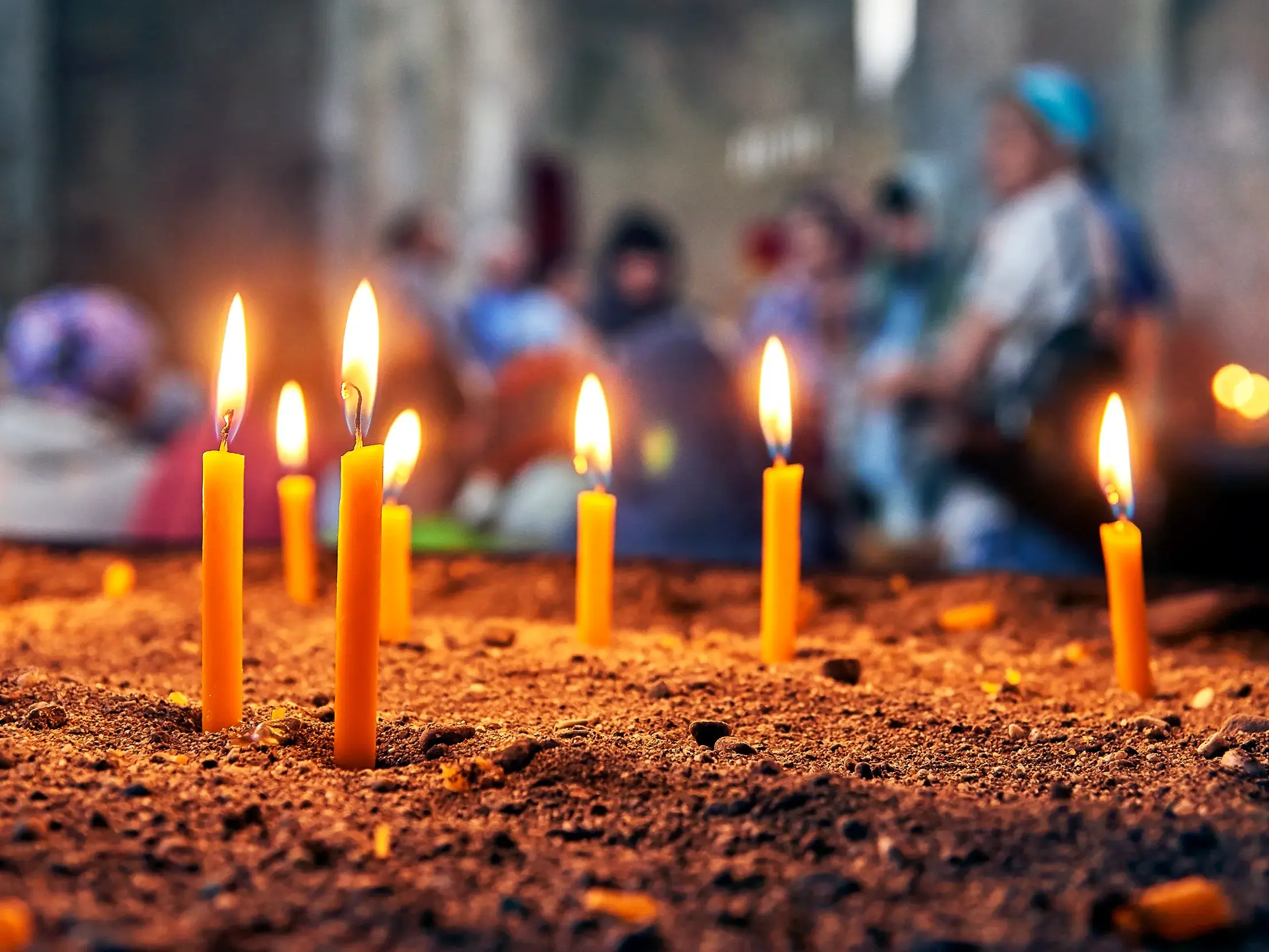 Leuchtende Votivkerzen in einem Sandbett in einer alten armenischen Kirche. Im unscharfen Hintergrund sind Gläubige zu sehen.