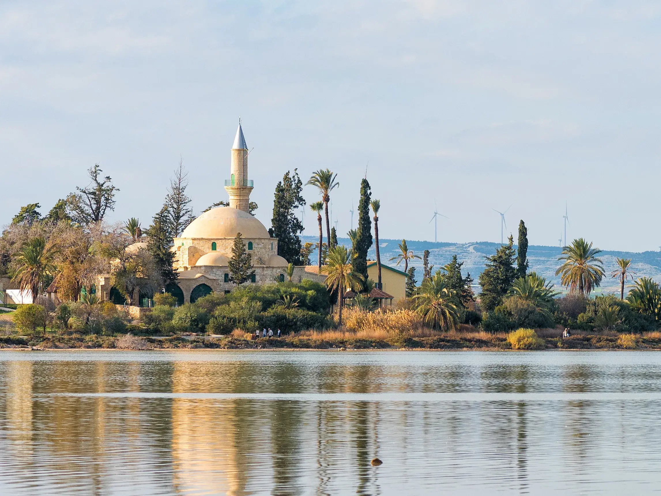 Die historische Moschee Hala-Sultan-Tekke am Salzsee von Larnaka, umgeben von Palmen, spiegelt sich im ruhigen Wasser.
