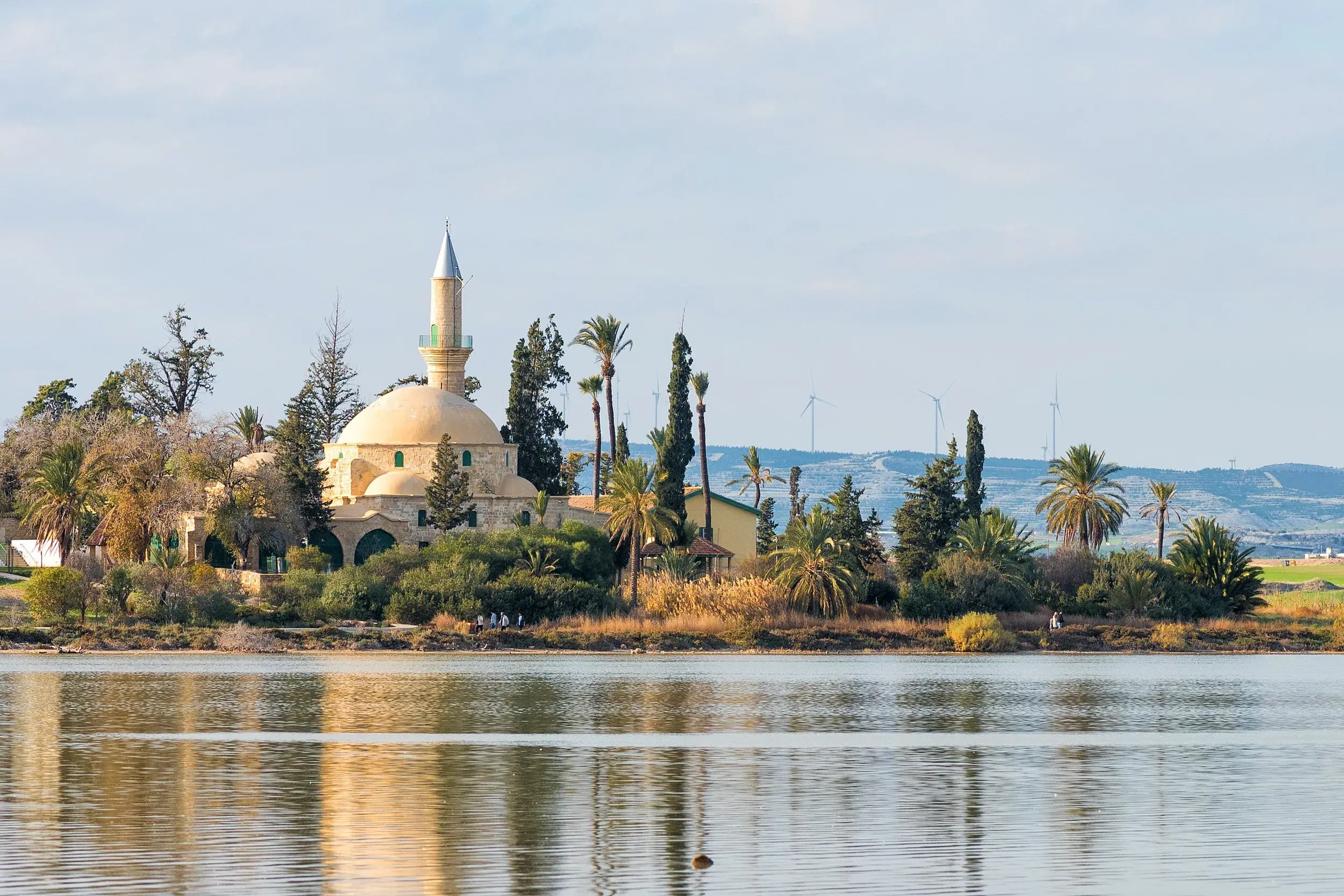 Die historische Moschee Hala-Sultan-Tekke am Salzsee von Larnaka, umgeben von Palmen, spiegelt sich im ruhigen Wasser.