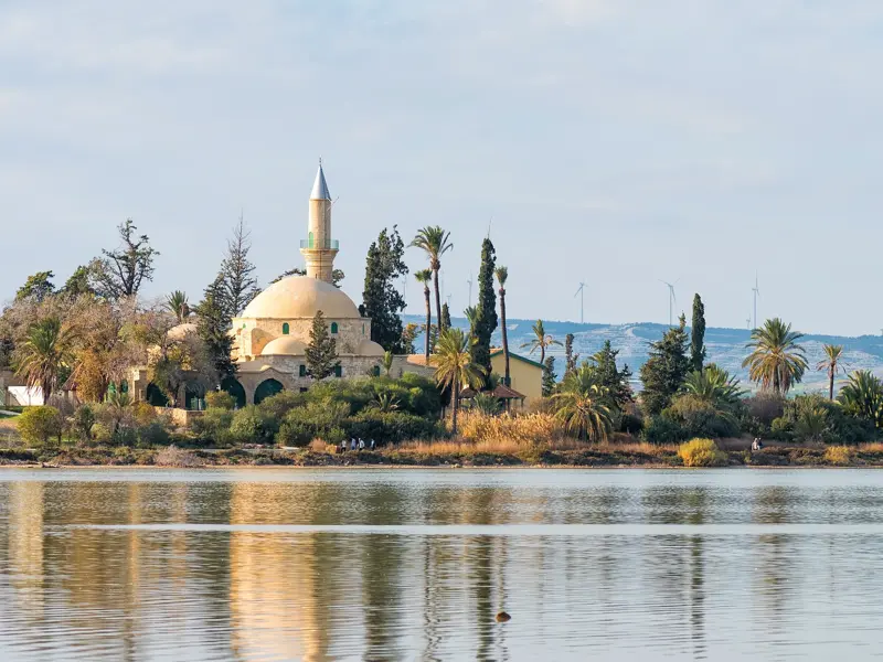 Die historische Moschee Hala-Sultan-Tekke am Salzsee von Larnaka, umgeben von Palmen, spiegelt sich im ruhigen Wasser.