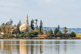 Die historische Moschee Hala-Sultan-Tekke am Salzsee von Larnaka, umgeben von Palmen, spiegelt sich im ruhigen Wasser.