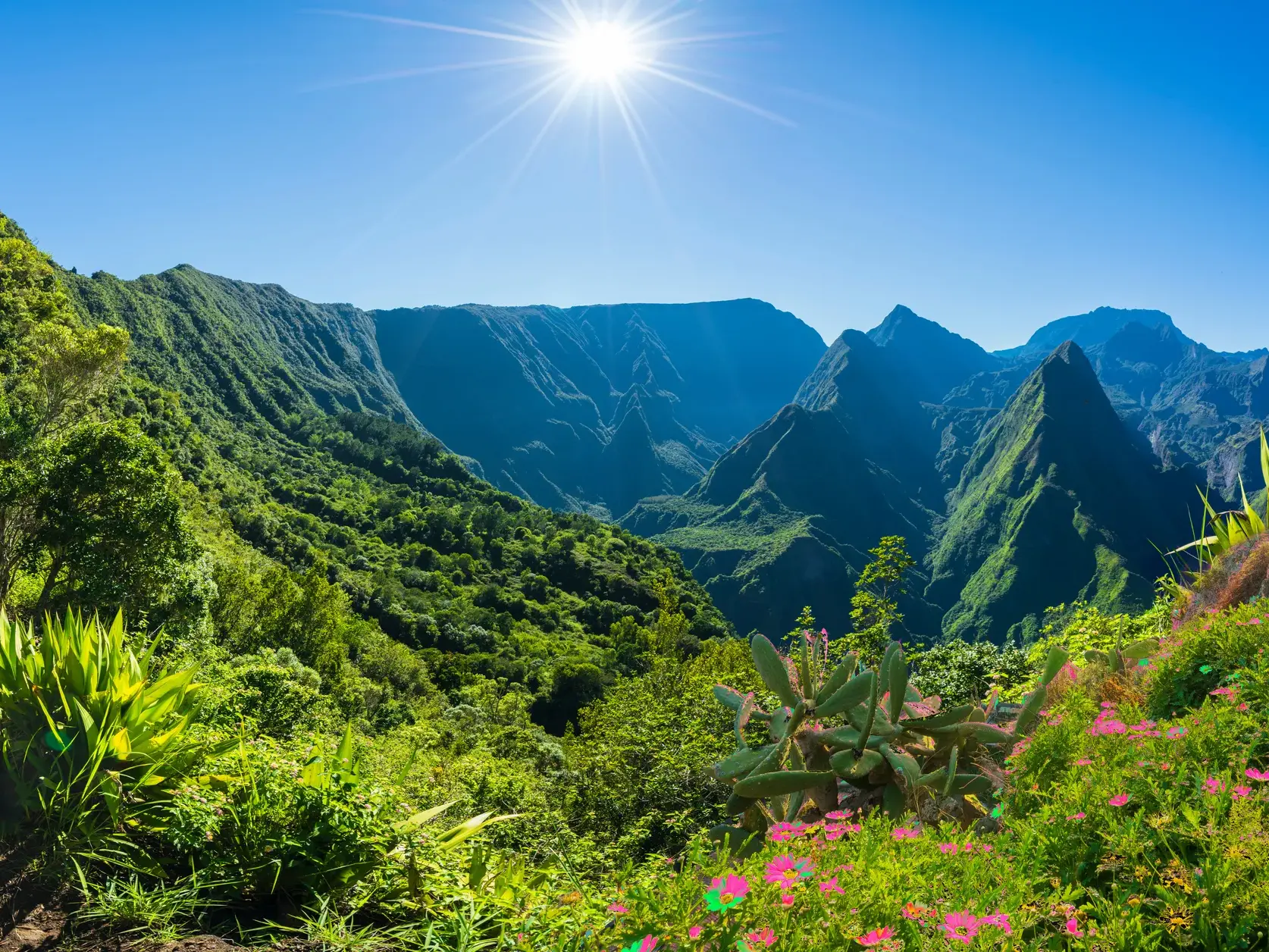 Strahlende Sonne über der üppig grünen Vulkanlandschaft des Mafate-Talkessels auf La Réunion bei einer Trekking-Tour.