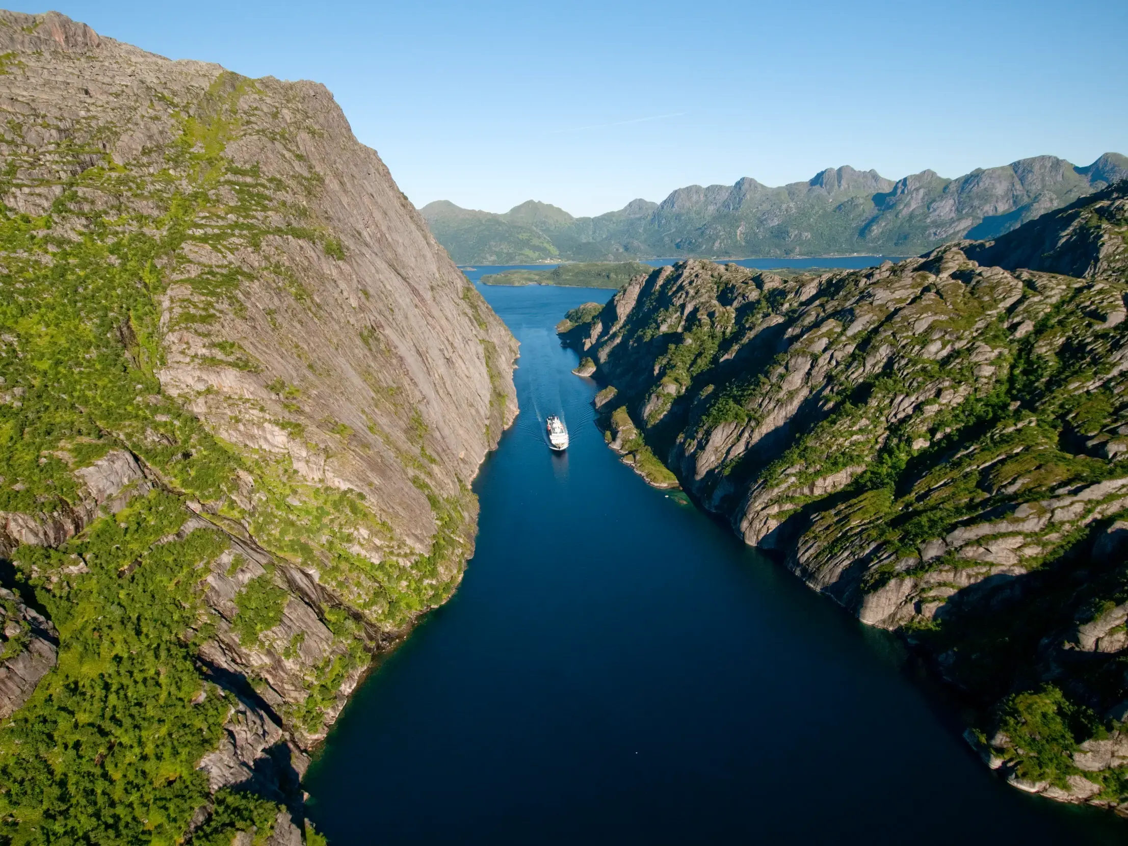 Ein Postschiff der Hurtigruten navigiert durch den schmalen Trollfjord in Norwegen, umgeben von steilen, grünen Felswänden.