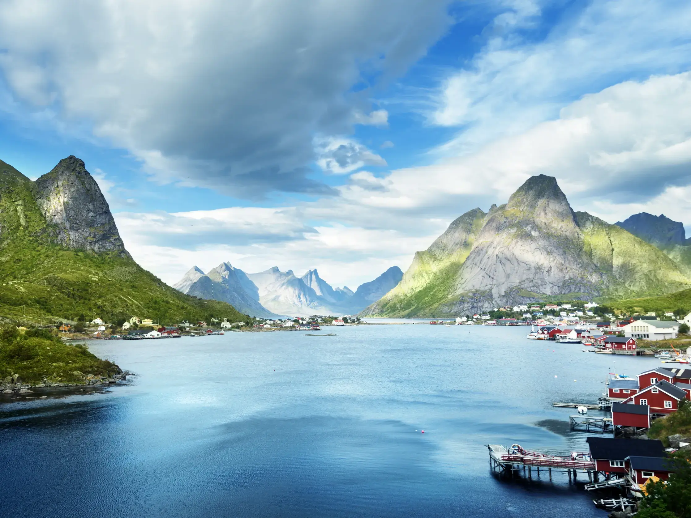 Typisch Lofoten - ein Ort umgeben von steilen, grünen Bergen am Ufer eines tiefblauen Fjords.