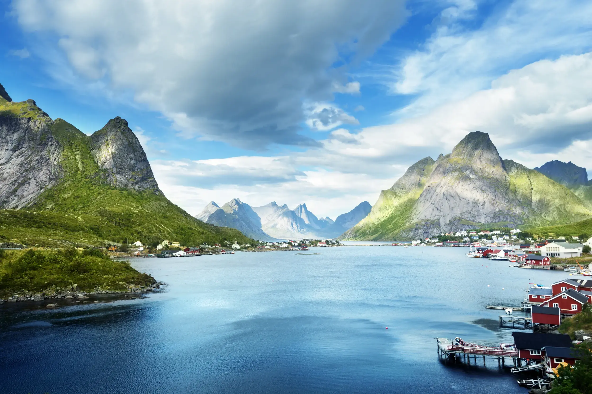 Typisch Lofoten - ein Ort umgeben von steilen, grünen Bergen am Ufer eines tiefblauen Fjords.