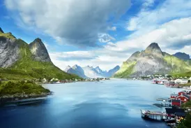 Typisch Lofoten - ein Ort umgeben von steilen, grünen Bergen am Ufer eines tiefblauen Fjords.