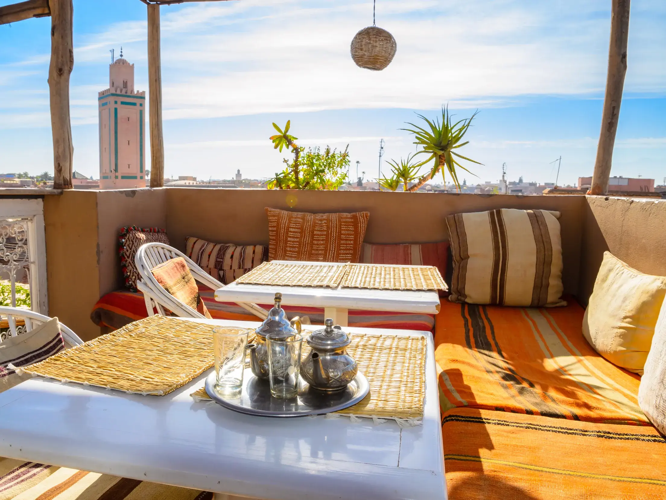 Traditioneller Minztee auf einer sonnigen Riad-Dachterrasse mit gemütlichen Polstern und Blick auf die Koutoubia-Moschee in Marrakesch.