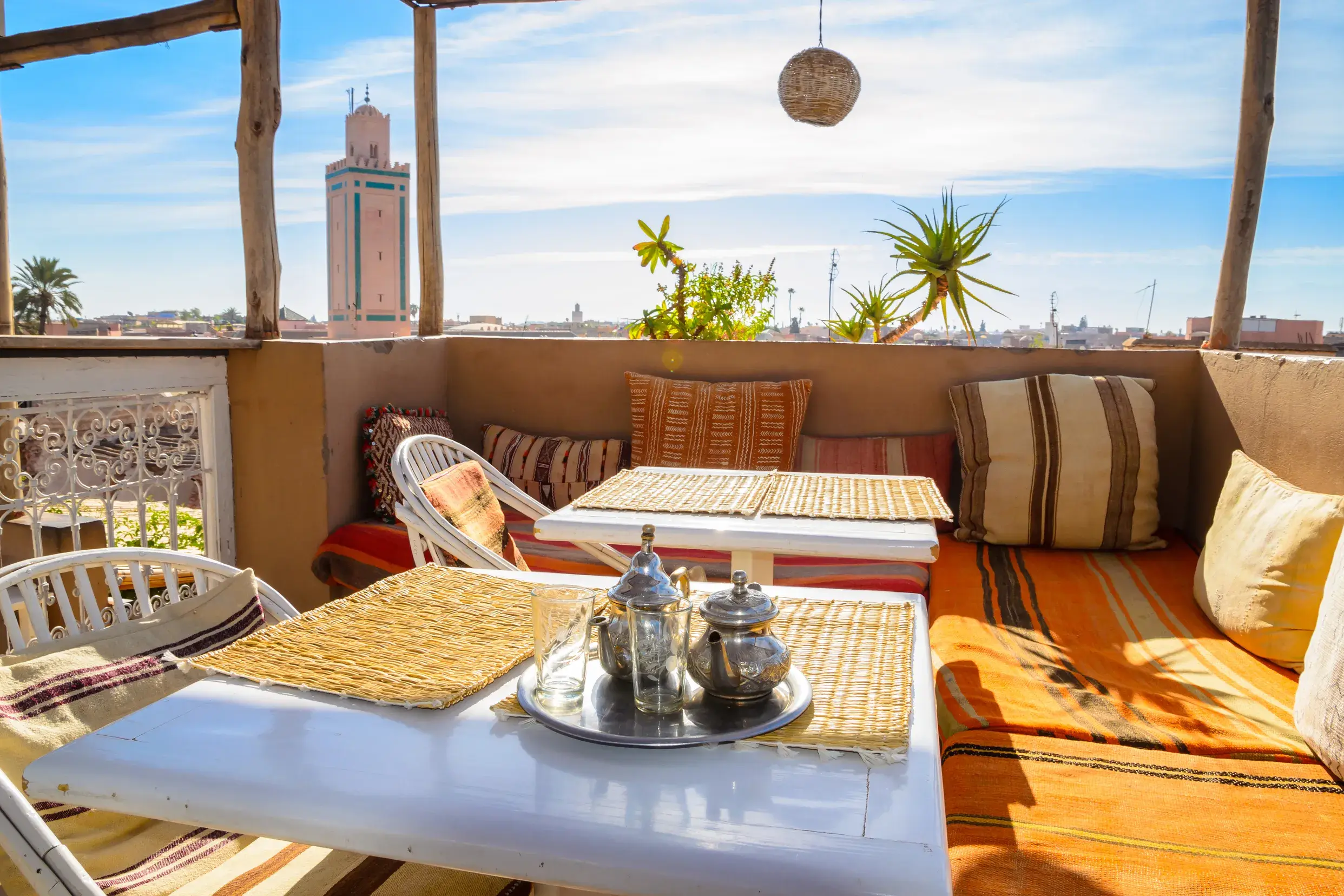Traditioneller Minztee auf einer sonnigen Riad-Dachterrasse mit gemütlichen Polstern und Blick auf die Koutoubia-Moschee in Marrakesch.