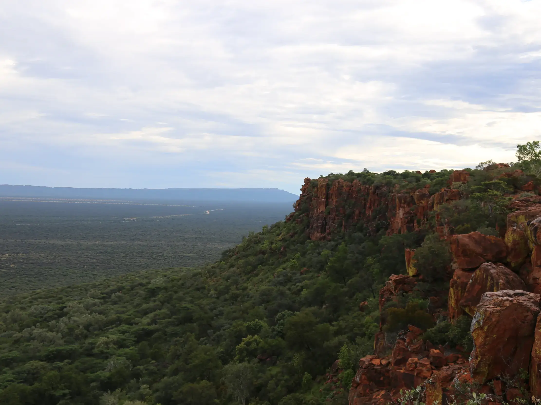 Wanderung auf dem Waterberg Plateau mit Blick von roten Sandsteinfelsen über die weite, grüne Savanne Namibias.