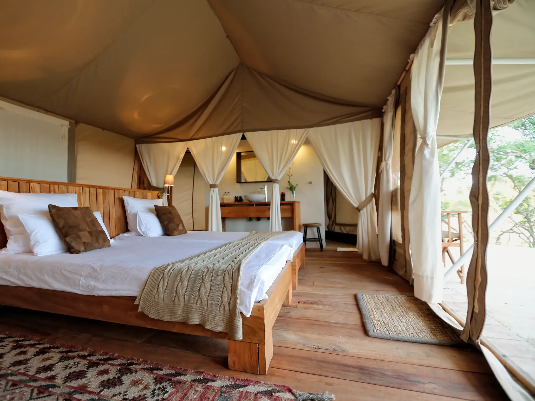 Luxuriöses Safarizelt mit Holzbett und Blick ins Bad im Maweninga Camp im Tarangire-Nationalpark, Tansania.