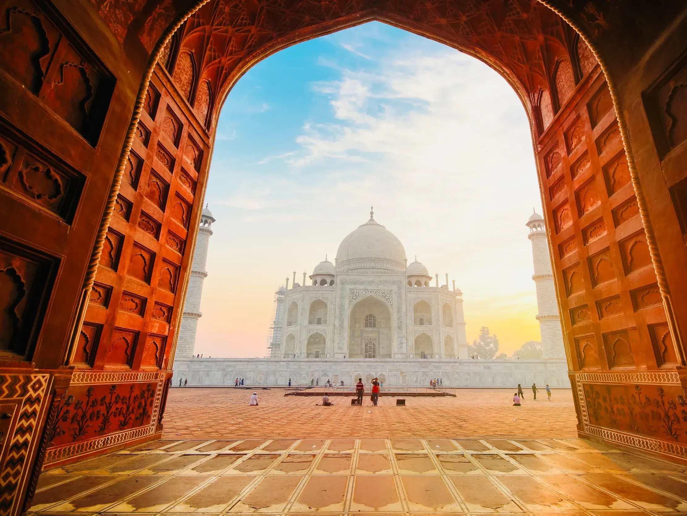 Ein großes, offenes Tor gibt den Blick frei auf das berühmte Taj Mahal in Agra, beleuchtet vom goldenen Licht des Sonnenaufgangs.