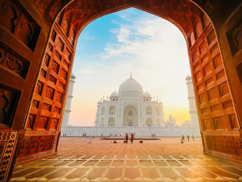 Ein großes, offenes Tor gibt den Blick frei auf das berühmte Taj Mahal in Agra, beleuchtet vom goldenen Licht des Sonnenaufgangs.