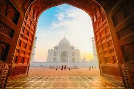 Ein großes, offenes Tor gibt den Blick frei auf das berühmte Taj Mahal in Agra, beleuchtet vom goldenen Licht des Sonnenaufgangs.