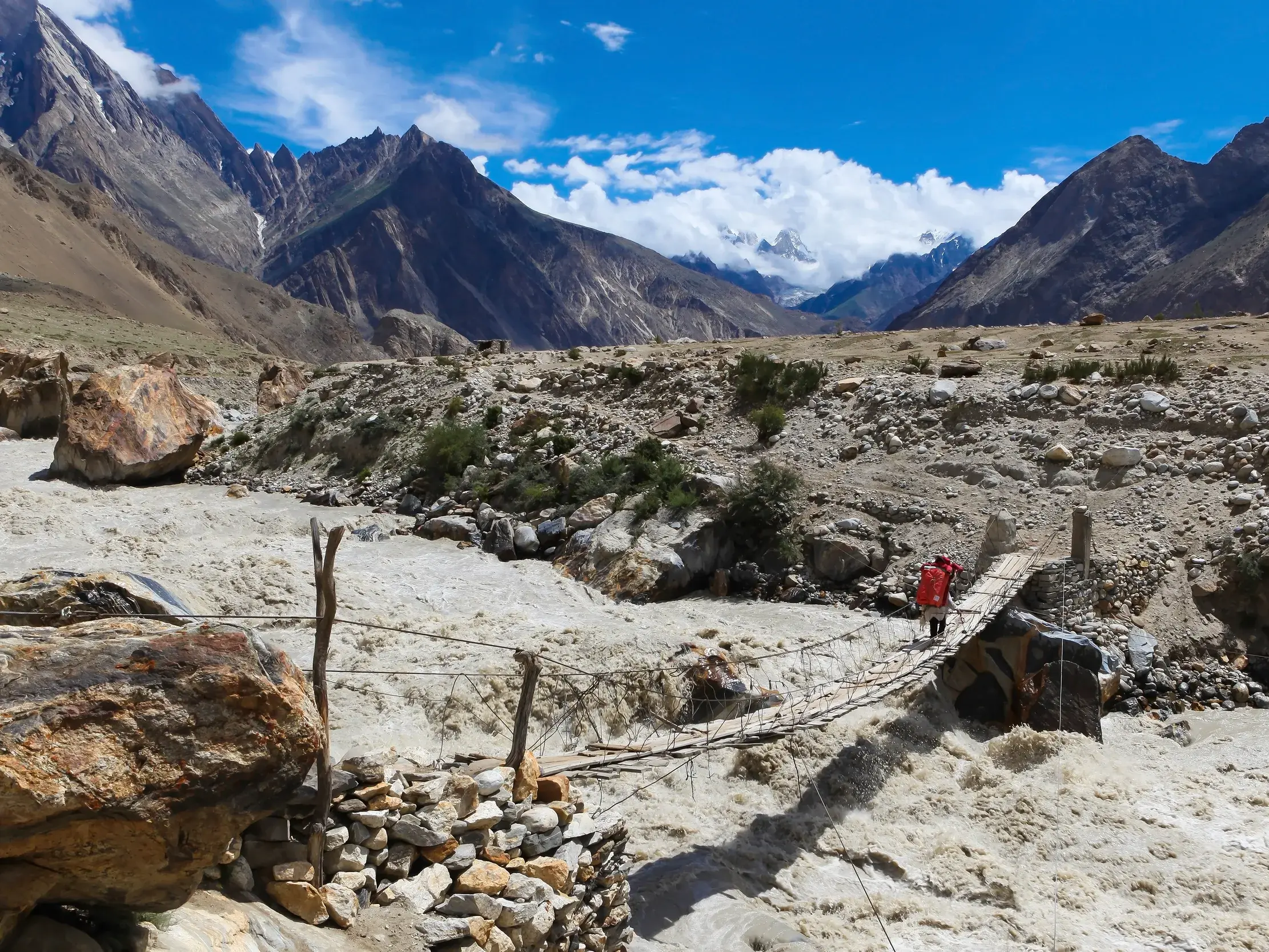 Trekker überquert eine abenteuerliche Hängebrücke über einen reißenden Fluss in der rauen Bergwelt des Karakorum in Pakistan.