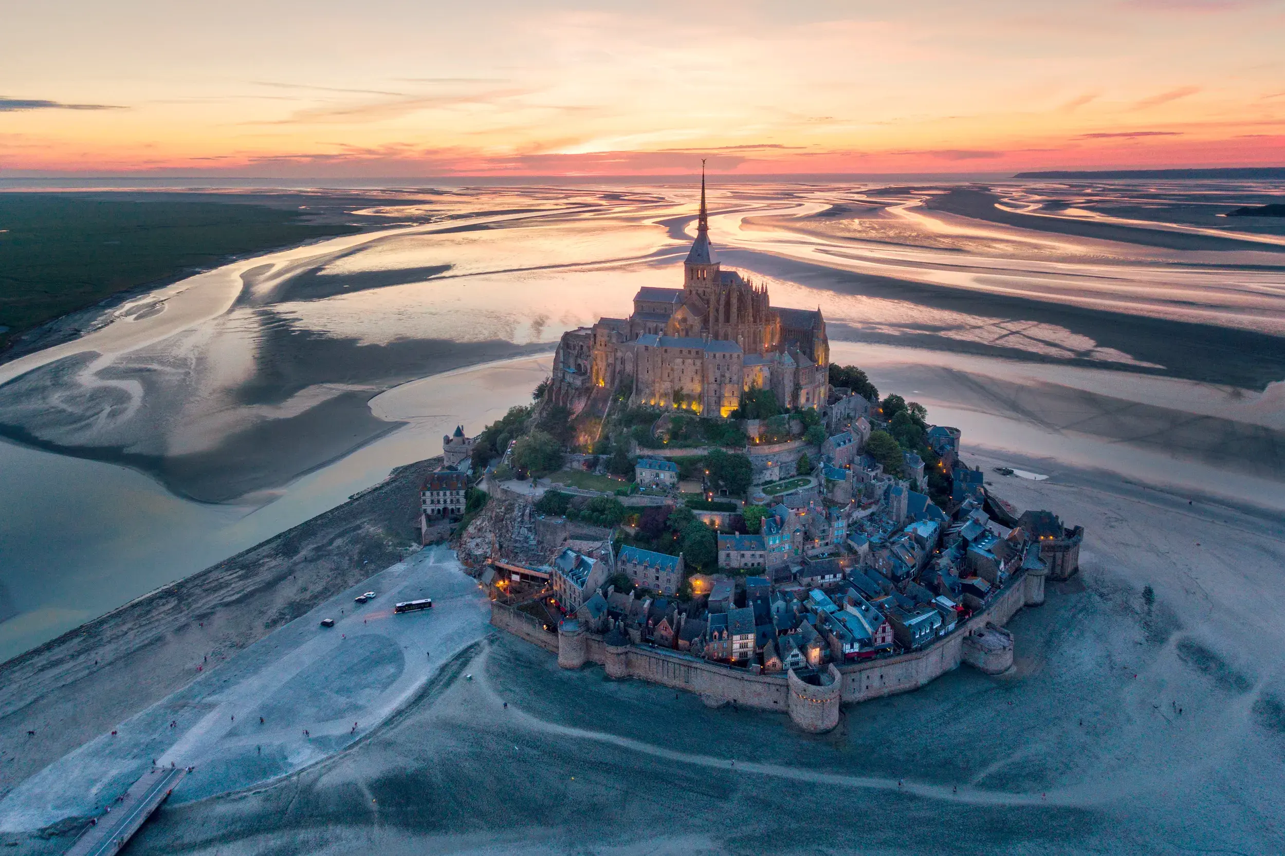 Der beleuchtete Mont St-Michel bei Sonnenuntergang. Luftaufnahme der Abtei in der Bretagne, umgeben von weitem Watt bei Ebbe.