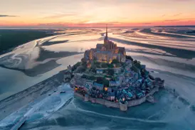 Der beleuchtete Mont St-Michel bei Sonnenuntergang. Luftaufnahme der Abtei in der Bretagne, umgeben von weitem Watt bei Ebbe.