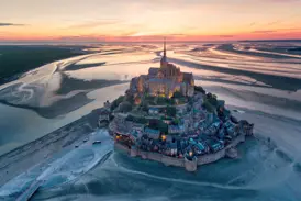 Der beleuchtete Mont St-Michel bei Sonnenuntergang. Luftaufnahme der Abtei in der Bretagne, umgeben von weitem Watt bei Ebbe.