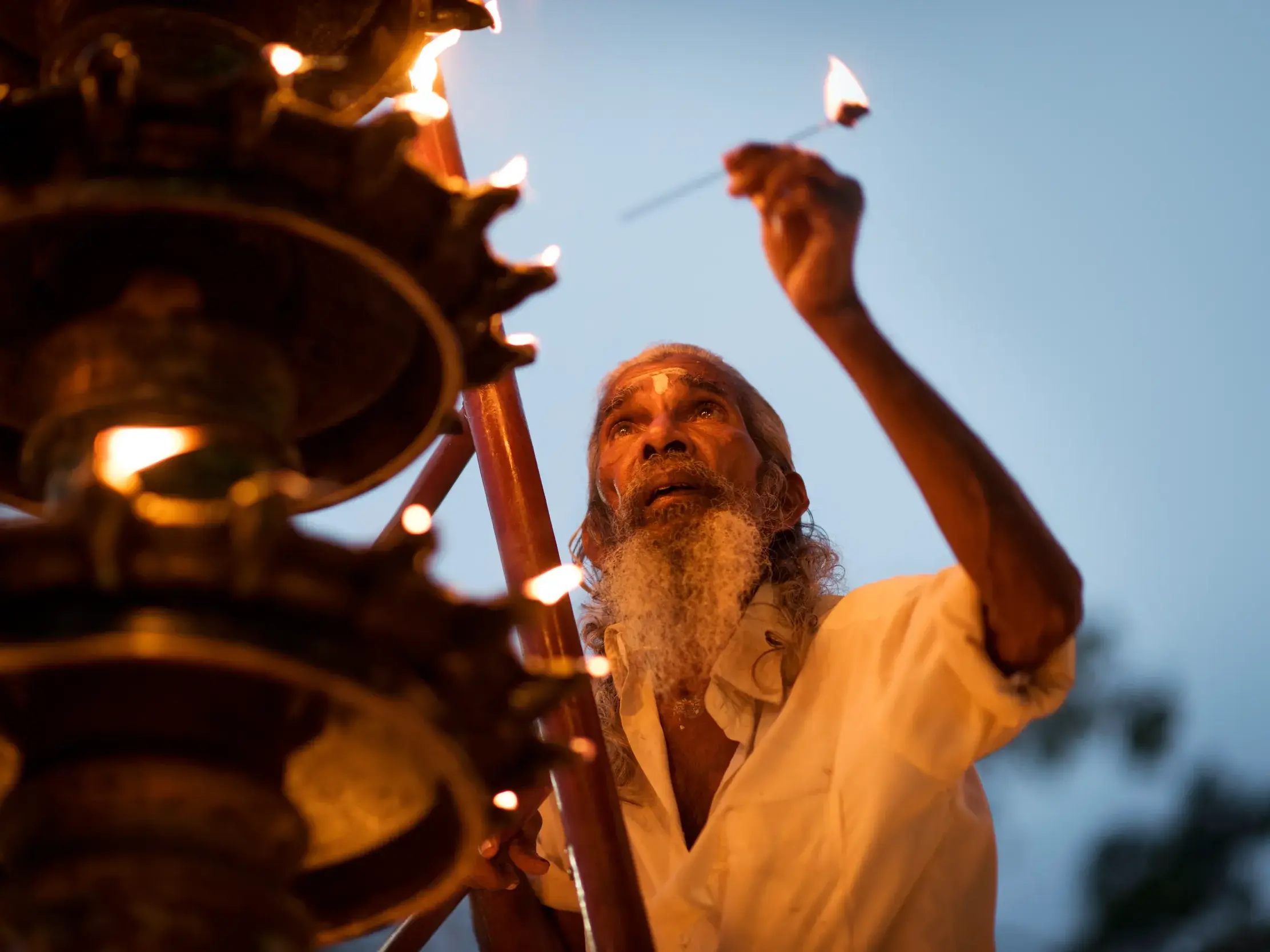 Ein Priester mit weißem Bart entzündet bei einer Abendzeremonie im Minakshi-Tempel in Madurai rituelle Öllampen.