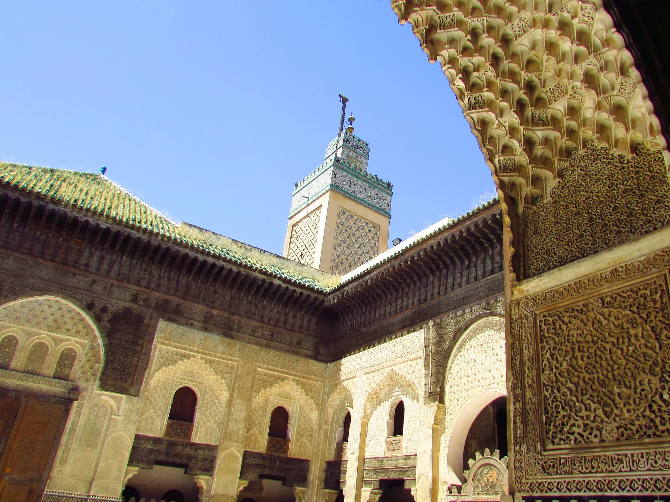 Blick durch einen reich verzierten Bogen in den sonnigen Innenhof der Medersa Bou Inania in der Königsstadt Fès.