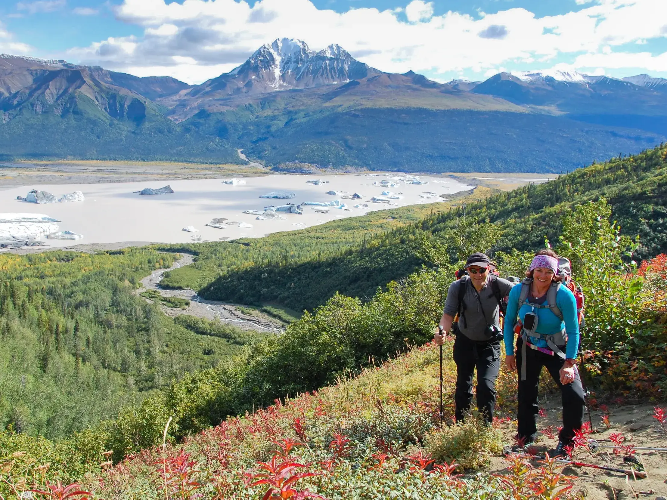 Zwei Wanderer auf einer Trekkingtour im Matanuska Valley in Alaska mit Blick auf den von Eisbergen bedeckten Gletschersee.