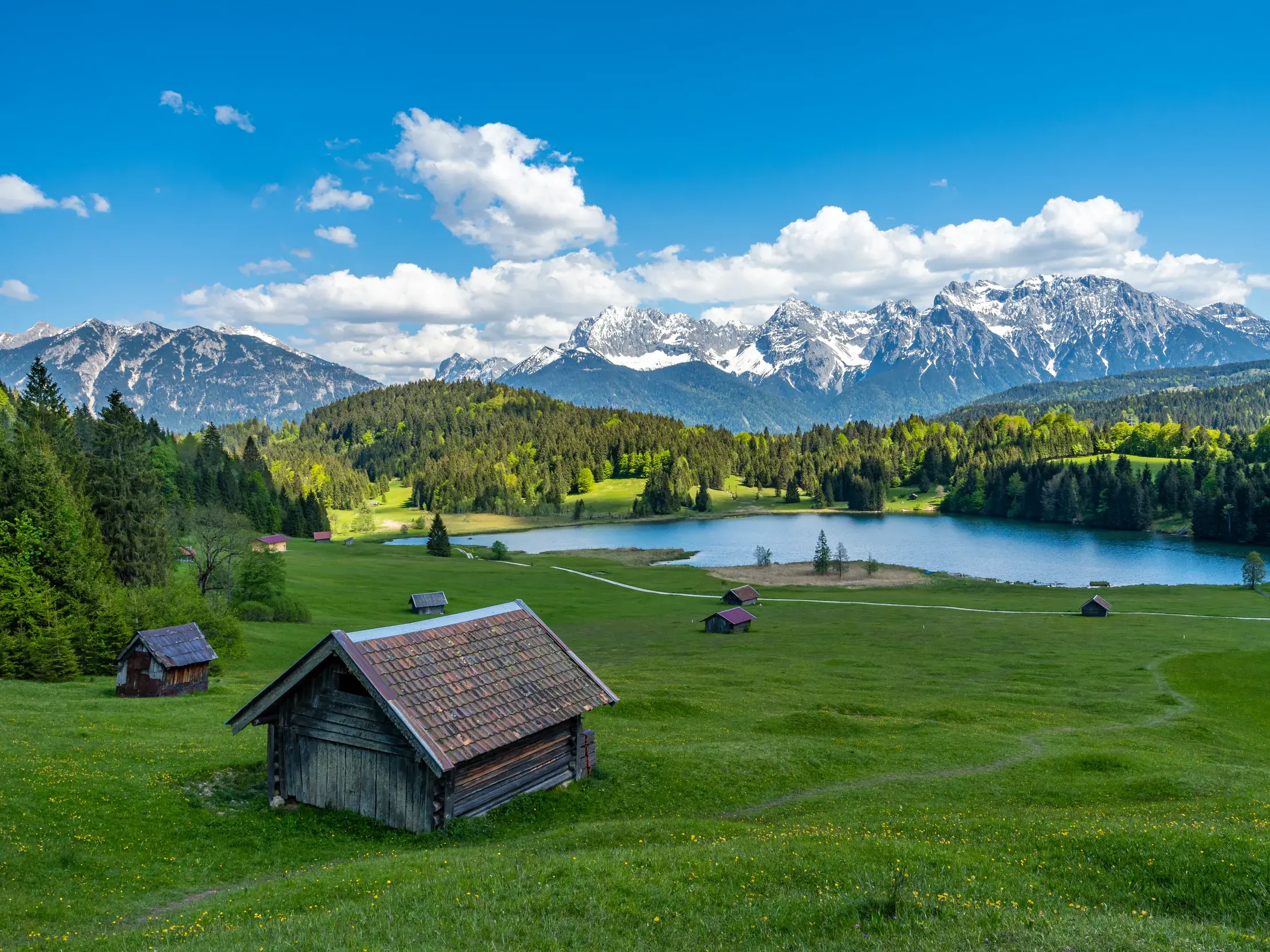 Sonnige Almwiese mit Holzhütte am Geroldsee und Panoramablick auf die schneebedeckten Gipfel des Karwendelgebirges.