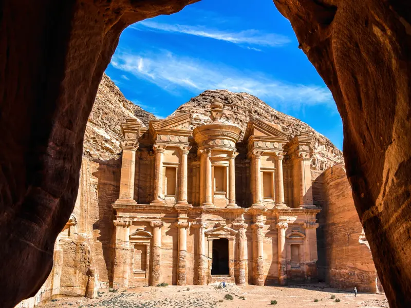 Das monumentale Felsenkloster Ed-Deir in Petra, gesehen durch einen Felsbogen bei strahlend blauem Himmel in Jordanien.