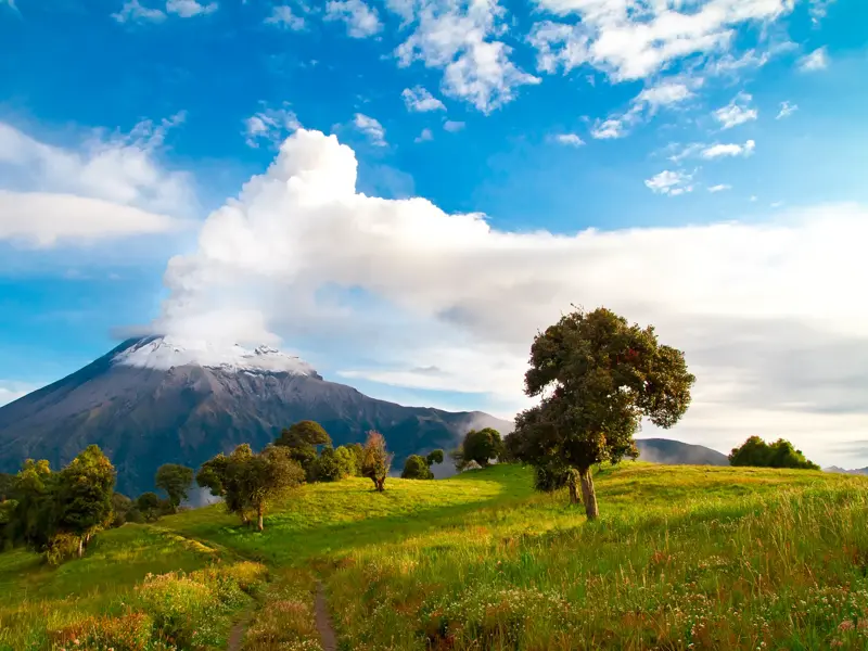 Der aktive Vulkan Tungurahua an Ecuadors Allee der Vulkane, dessen Rauchwolke über einer grünen, sonnigen Hügellandschaft aufsteigt.