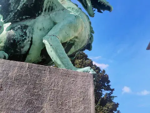 Nahaufnahme einer der vier berühmten Drachenstatuen auf der Drachenbrücke, dem Wahrzeichen von Ljubljana, vor blauem Himmel.