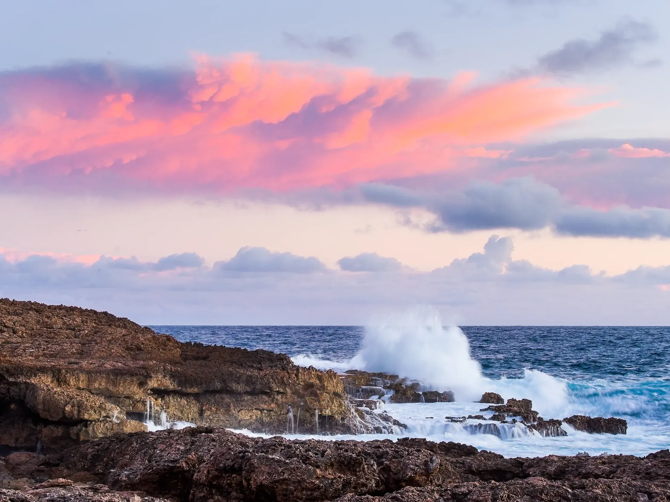 Wellen des karibischen Meeres brechen an der zerklüfteten Felsküste der Pointe des Chateaux auf Guadeloupe bei Sonnenuntergang.